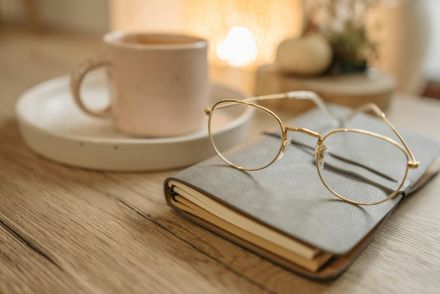 Close-up of stylish eyeglasses on a notebook with a coffee cup in soft lighting.