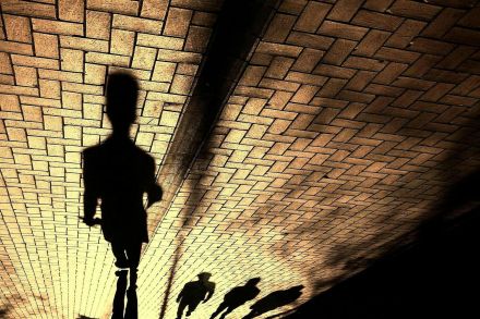 Dramatic shadows of people walking on a brick pavement, showcasing abstract human silhouettes.